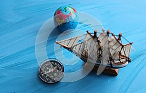 Sea Travel Concept Image. Globe, Wooden Ship Model And Vintage Compass On Blue Surface Symbolizing Ocean