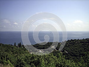 Sea view from the coastal mountains. The coastal hills are surrounded by dense vegetation, including low buildings. In the