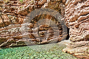 The sea view. Entrance to the cave from the sea. Calm clear sea. The rock consists of layered stones. Montenegro