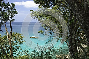 Sea view and traditional Thai boat through rainforest. Round large stones and azure clear water.