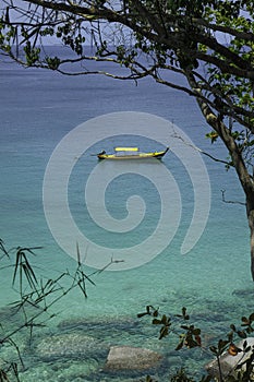 Sea view and traditional Thai boat through rainforest. Round large stones and azure clear water.