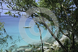 Sea view and traditional Thai boat through rainforest. Round large stones and azure clear water.