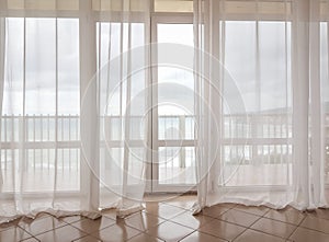 Sea view through a transparent curtain on a huge panoramic window with a balcony, modern interior of apartments in a