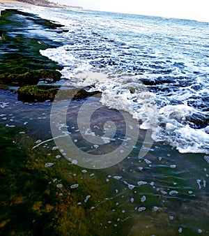 sea water coving a huge green stone at the Seashore.