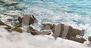 Sea water illuminated by sunlight washes big rocks on beach