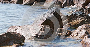 Sea water rolls onto rocky shore with boulders Splash, drop Wild deserted beach