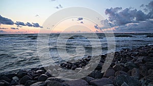 The sea wave alternatively crashes against the rocky beach at sunset. Seascape