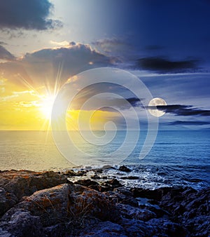 sea wave attacks the boulders of rocky shore with sun and moon at twilight
