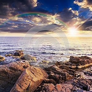 Sea wave breaks about boulders with rainbow