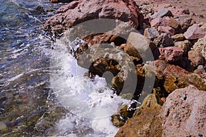 A sea wave with foam hits the stone shore.