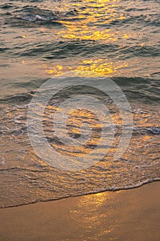 Sea wave foam on sandy beach in sundown light, close up. Tropical summery background