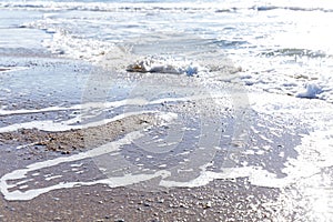 Sea wave with foam on the sandy shore on a sunny day. Rest and relaxation at the resort. Space for text. Background