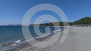 The sea wave, foaming, rolls onto the sandy-pebble beach, which stretches towards the islands along the coast with pine trees grow