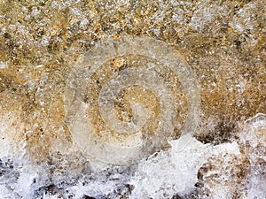 Sea wave mixes with sand, sea foam, water splash. Top view. Beach sunset abstract background