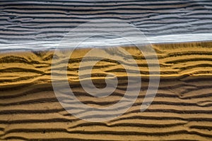 Sea-wave murals in the sand of the coast through a water magnifier