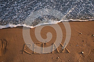 Sea wave rolling onto sandy beach with written word Relax, above view