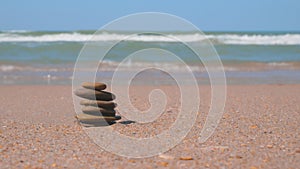 The sea wave rolls on the sandy shore. A stack of pebbles are stacked in a pyramid. Zen meditation, harmony, balance