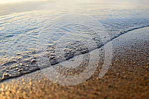 Sea wave and sand seashore. Golden sun light over the sea ocean waves. MIrror reflection on water surface. Macro close up