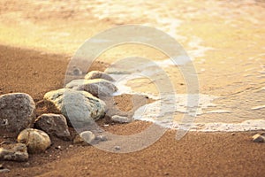 Sea wave on sand and stone at sunrise