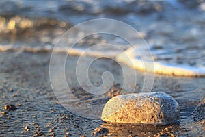 Sea wave on sand and stone at sunrise