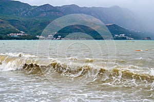 Sea wave in stormy weather. The turbid wave. Low clouds over the coast. Montenegrin beach in rainy weather. The sea and mountains