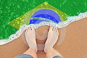 Sea wave on the sunny sandy beach with flag Brazil. Top View on Feet in the sand