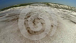 Sea wave with white foam rolls over sandy shore of beach. Top view.