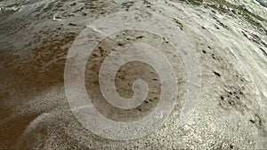 Sea wave with white foam rolls over sandy shore of beach. Top view.