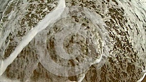 Sea wave with white foam rolls over sandy shore of beach. Top view.