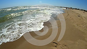 Sea wave with white foam rolls over sandy shore of beach. Top view.