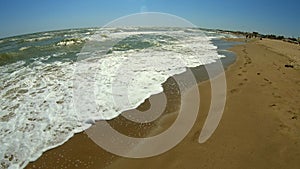 Sea wave with white foam rolls over sandy shore of beach. Top view.