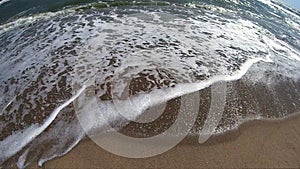 Sea wave with white foam rolls over sandy shore of beach. Top view.