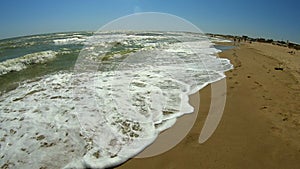 Sea wave with white foam rolls over sandy shore of beach. Top view.