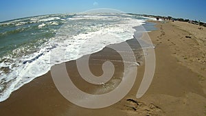 Sea wave with white foam rolls over sandy shore of beach. Top view.