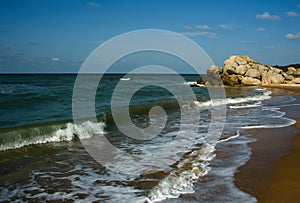 Sea waves break into small splashes on the coastal rocks.