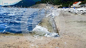 Sea waves breaking on the pier with sunbeds and stepladders leading to the water on a cold windy day at sea resort