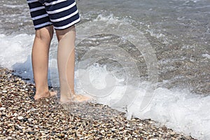 Sea waves and coastline. Little boy`s legs in the picture.