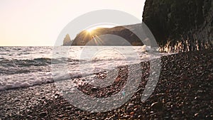 Sea waves crash on the rocky coast at sunset