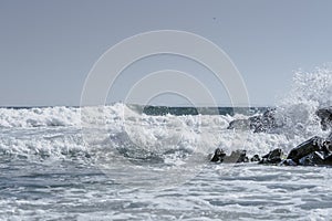 Sea waves crashing on beach rocks with simple horizon and clear sky. Splashing waves on beach.