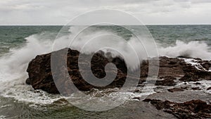 Sea waves crashing hard against a rock in winter