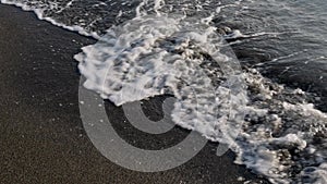 Sea waves and foam on black sand. Beach and relaxation