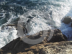 Sea waves with foam on the rock coast at sunlight