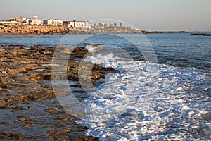 Sea waves with foam on the stony shore. Mediterranean town in th