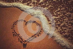 Sea waves and heart drawing on the sand beach near the ocean. Summer love concept.