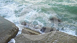 Sea waves hit rocks and stones with splashes in slow motion