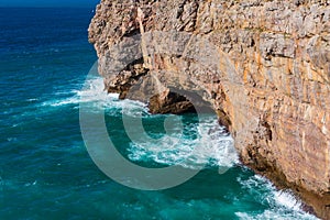 Sea waves hitting rock cliff with a cave at Fortaleza de Sagres, Portugal