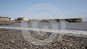 Sea and waves lapping on pebbles Minehead harbour Somerset England with boats in summer