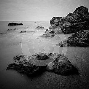 Sea waves lash line impact rock on the beach. Black and white photography.