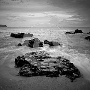 Sea waves lash line impact rock on the beach. Black and white photography.