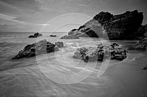 Sea waves lash line impact rock on the beach. Black and white photography.